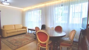 A living room with a beige sofa, a dining table with four chairs, and a patterned rug.