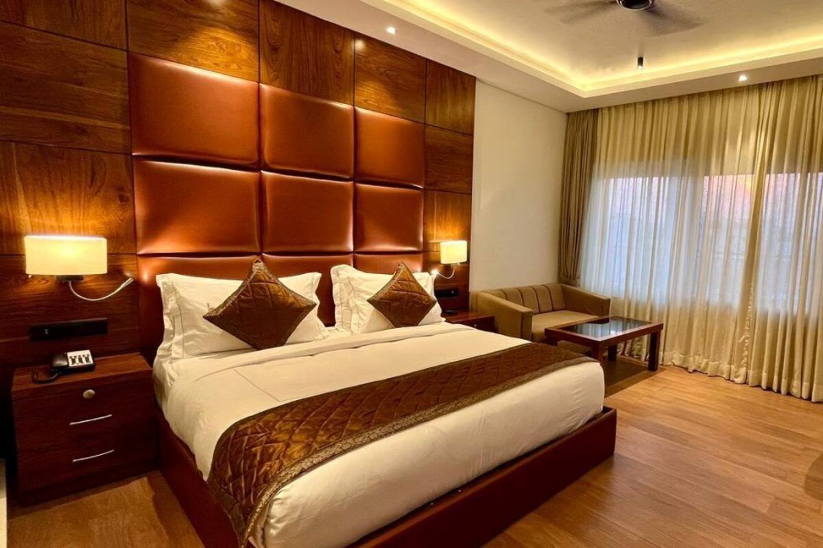 Ein Hotelzimmer mit einem großen Bett, einem Holz-Kopfende, zwei Nachttischen mit Lampen, einem kleinen Schreibtisch mit Stuhl und einem großen Fenster mit Vorhängen.
