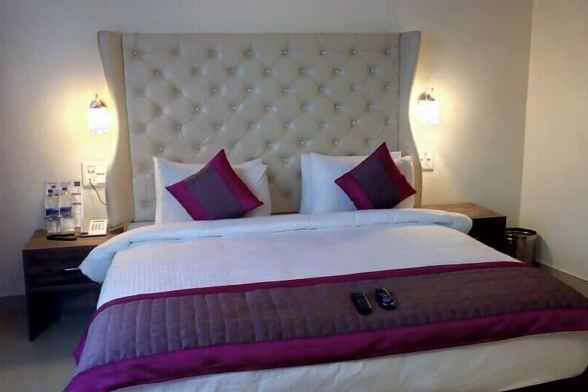 Ein Hotelzimmer mit einem großen Bett, zwei Nachttischen und einem mit Wirbelstickereien versehenen Kopfteil.