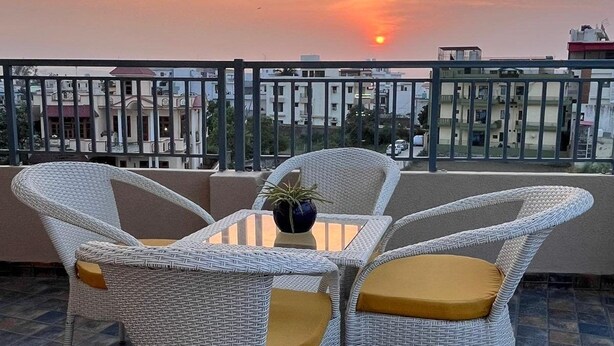 Un balcon avec des fauteuils en osier et une table, une plante en pot et une vue sur le coucher de soleil.