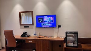 Une chambre d’hôtel avec un bureau en bois, un téléviseur fixé au mur, un réfrigérateur et une fenêtre avec des rideaux.