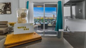 Een moderne woonkamer met een glazen salontafel, een bord met de tekst 'THANK YOU', een bank en uitzicht op een stadsbeeld door een schuifpui.