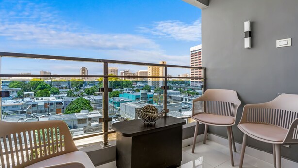 Een balkon met uitzicht op de stad, twee stoelen, een kleine tafel en een decoratief object.