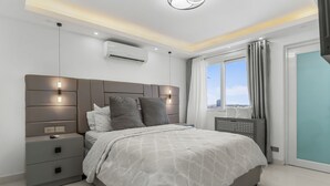 Een moderne slaapkamer met een groot bed, nachtkastjes, een airconditioning en uitzicht op de stad.