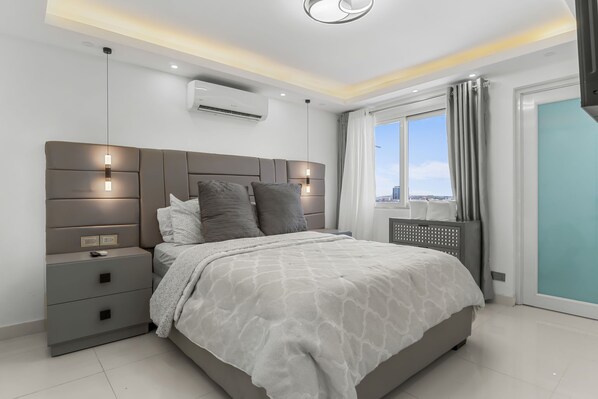 Ein modernes Schlafzimmer mit einem großen Bett, Nachttischen, einer Klimaanlage und Blick auf die Stadt.