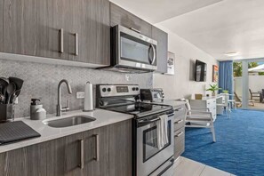 Cocina moderna con microondas, estufa y lavamanos. Hay una zona de comedor con mesa y sillas.