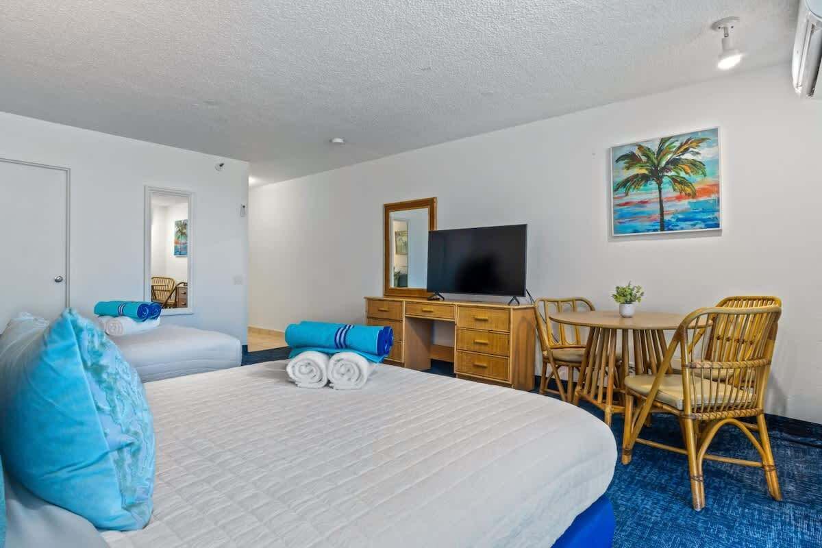 Une chambre d’hôtel avec un grand lit, un bureau avec un ordinateur, une télévision et une petite table avec des chaises.