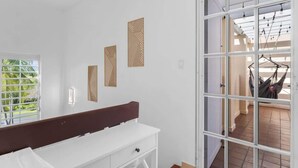 A room with a white bench, a window with blinds, and a view of an outdoor area with a hammock. - Studio w/ King Bed & Balcony (Palmas del Mar)