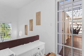 A room with a white bench, a window with blinds, and a view of an outdoor area with a hammock. - Studio w/ King Bed & Balcony (Palmas del Mar)