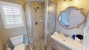Ein Badezimmer mit Duschkabine, Toilette, Waschbecken mit Spiegel und Fenster mit Jalousien.