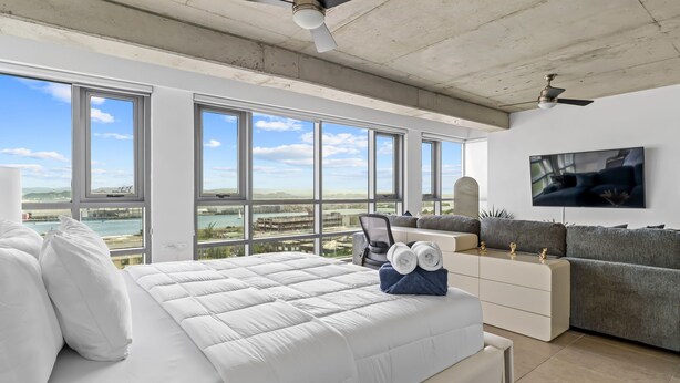 A modern bedroom with a large bed, a sofa, a TV, and a view of the sea. - Luxe Studio @ Atlantis | 5 Min to Old San Juan (San Juan)