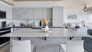 A modern kitchen with a central island, white cabinetry, and a dining area with two chairs. - Luxe Studio @ Atlantis | 5 Min to Old San Juan (San Juan)