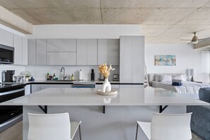 A modern kitchen with a central island, white cabinetry, and a dining area with two chairs.