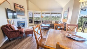 A spacious living room with a fireplace, a large wooden dining table, and a sofa set. - River Ridge 423a 2 Bedroom Condo (Bend)