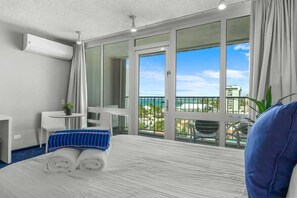 Une chambre d’hôtel avec un grand lit, un bureau, une chaise et un balcon donnant sur la mer.