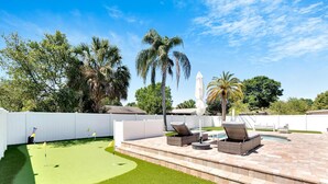 Un jardin avec une terrasse, des chaises longues, une petite piscine et un terrain d’entraînement au golf.