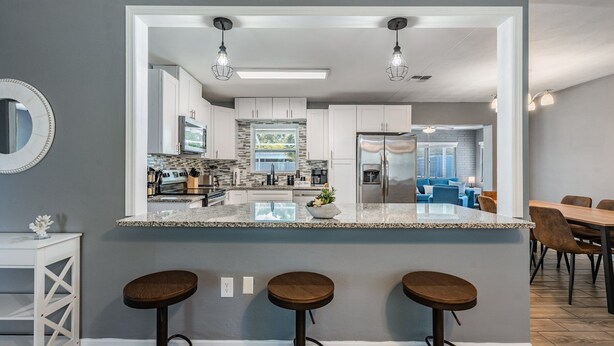 A modern kitchen with a central island, bar stools, and a dining area with a blue sofa. - 3442 Azalea Pl Summar (Largo)