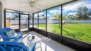 A covered patio with wicker furniture, a ceiling fan, and a view of a grassy yard and neighboring houses.