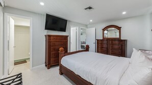 A bedroom with a wooden bed, a dresser, a television mounted on the wall, and a mirror above the dresser.