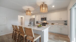 A modern kitchen with white cabinets, a central island, wicker bar stools, and pendant lighting. - 2405 E 19th Ave Summa (Tampa)