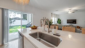 A modern kitchen with a large sink, a dining area with wicker furniture, and a TV mounted on the wall. - 2405 E 19th Ave Summa (Tampa)