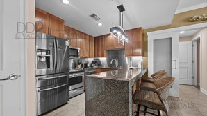 A modern kitchen with granite countertops, stainless steel appliances, and wooden cabinets. - Ocean Club 406 | Enjoy Views of the Gulf! (Biloxi)