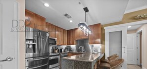 Une cuisine moderne dotée de plans de travail en granit, d’appareils électroménagers en acier inoxydable et d’armoires en bois.