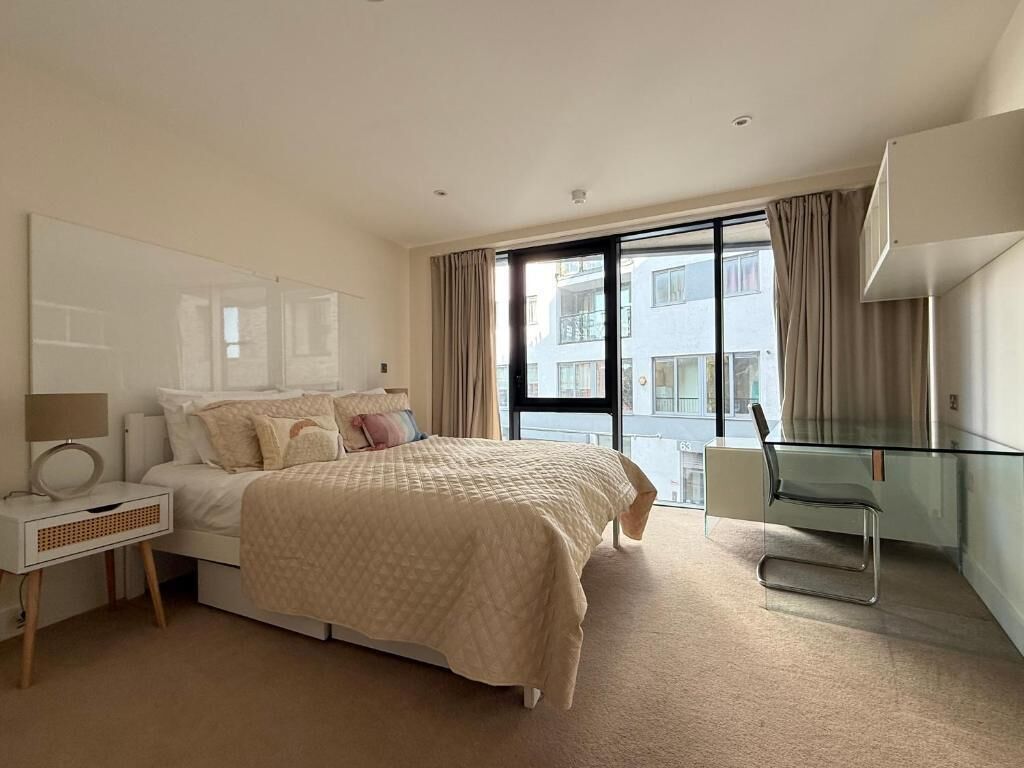 Quarto de hotel moderno com uma cama grande, uma mesa de vidro e vista da cidade através de amplas janelas.
