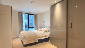 A modern bedroom with a large bed, a wardrobe, and a window with curtains.
