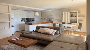 A modern living room with a large sectional sofa, a wooden coffee table, and a dining area with a white table and chairs.