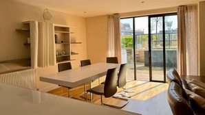 A modern dining area with a long table and chairs, a built-in bookshelf, and a sliding glass door leading to an outdoor patio.