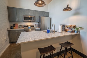 A kitchen with grey cabinets, stainless steel appliances, a granite countertop, and two stools.
