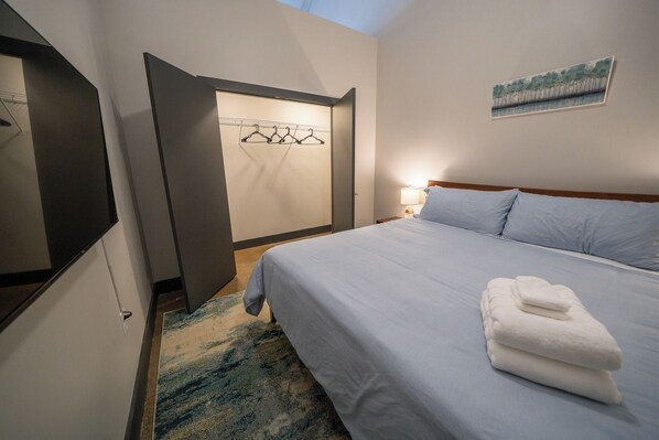 A hotel room with a bed, a wall-mounted coat rack, a painting, and a nightstand with a lamp.