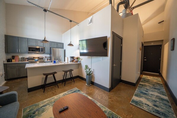 Una cocina moderna con una isla central, taburetes de bar, un televisor de pantalla plana y una zona de comedor con mesa y sillas.