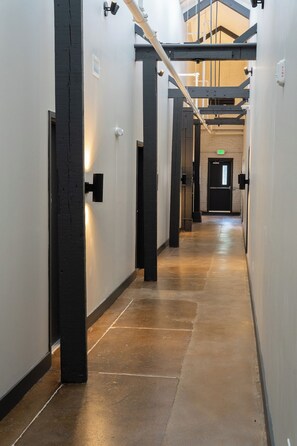 Un pasillo con piso de concreto pulido, paredes blancas y columnas estructurales negras.