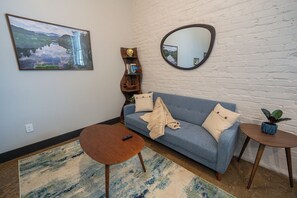 A living room with a sofa, a coffee table, a side table with a plant, a mirror, and a bookshelf.