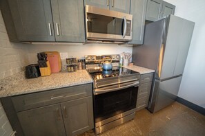 A kitchen with grey cabinets, a stainless steel microwave, a double oven, and a refrigerator.