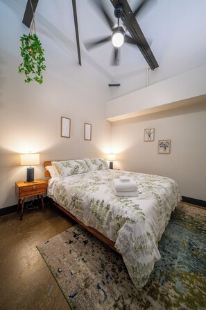 A bedroom with a bed, bedside lamps, a ceiling fan, and wall art.