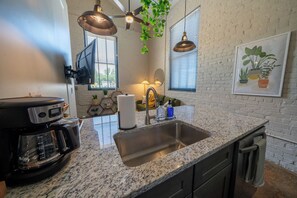 A kitchen with a coffee maker, sink, and pendant lights.
