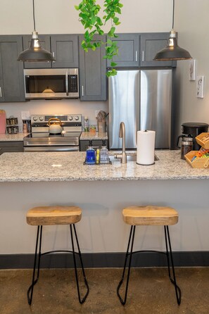 A modern kitchen with stainless steel appliances, granite countertops, and two wooden bar stools.