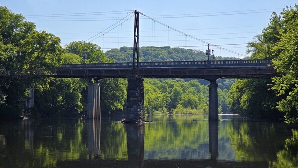 A bridge over a calm river with a forested hillside in the background.