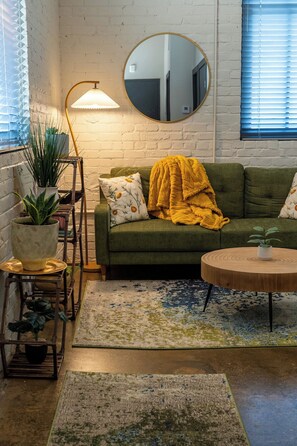 A cozy living room with a green sofa, a round wooden coffee table, and a variety of plants.