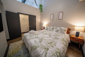 A bedroom with a bed, bedside tables, a wardrobe, and a hanging plant.