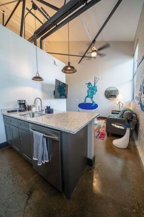 A modern kitchen with a large island, stainless steel appliances, pendant lighting, and a mural on the wall.