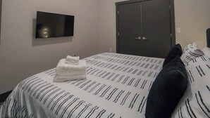 A hotel room with a bed, a flat-screen TV, a ceiling fan, and a dark door.