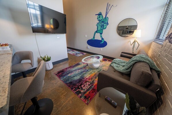 A modern living room with a flat-screen TV, a colorful rug, a sofa, a coffee table, and a wall mural.