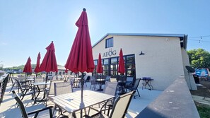 Un espace extérieur aménagé avec des tables et des chaises, des parasols rouges et un bâtiment portant l’inscription « AFOG ».
