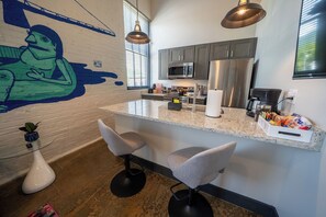 Une cuisine moderne dotée d’un îlot central, de tabourets de bar, d’appareils électroménagers en acier inoxydable et d’une fresque murale.