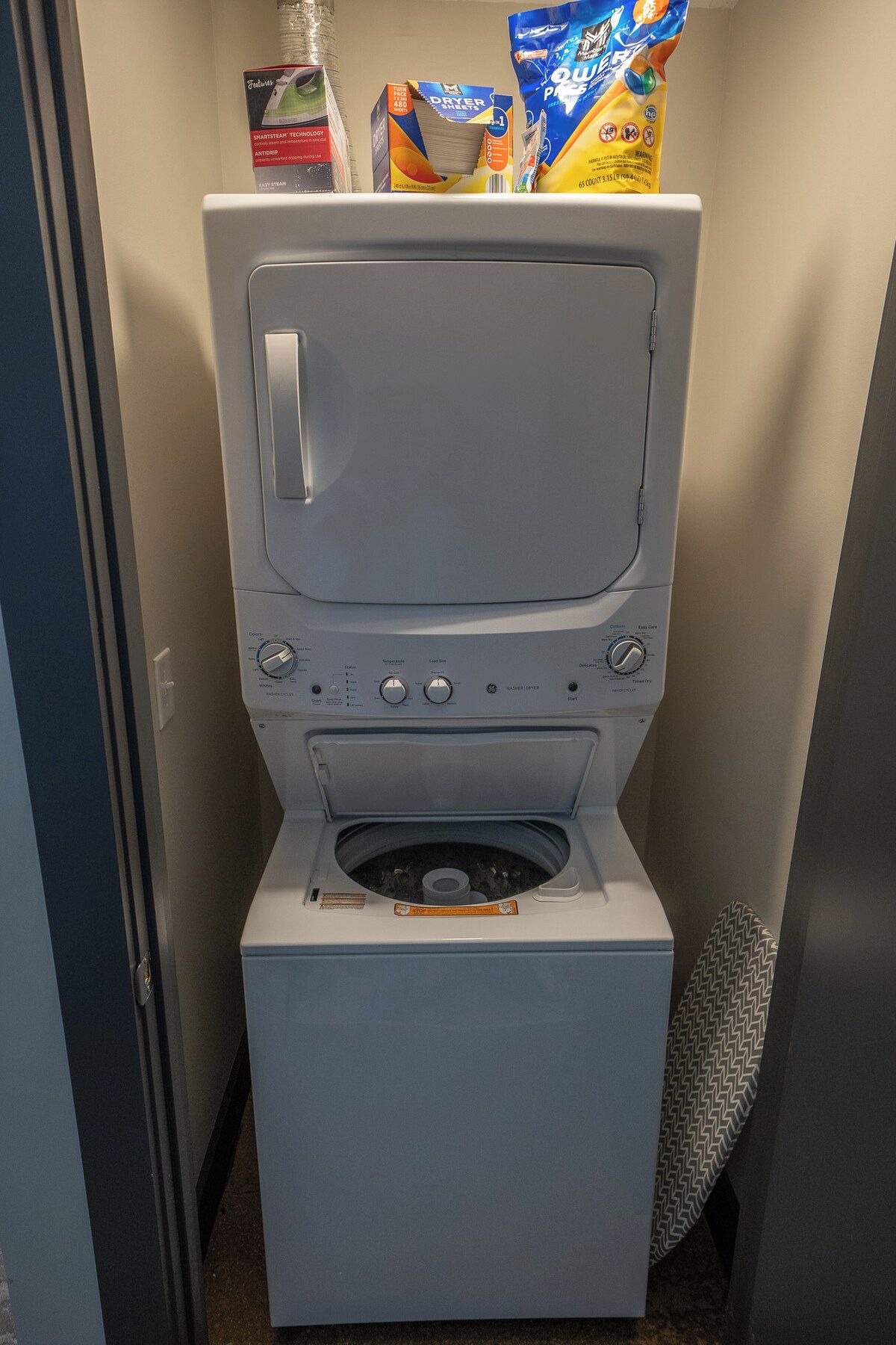 A compact, grey portable washer-dryer unit with a front-loading door, control panel with multiple settings, and a small storage compartment.