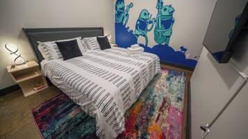 A bedroom with a bed, a nightstand, a wall-mounted TV, and a colorful rug.